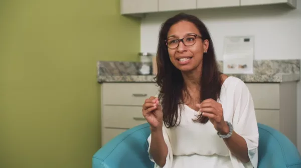 A woman in glasses sitting in a chair.