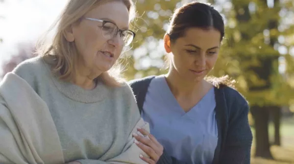 A nurse and an older woman walking in a park.