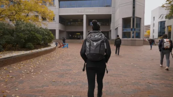A woman with a backpack walking down a sidewalk.