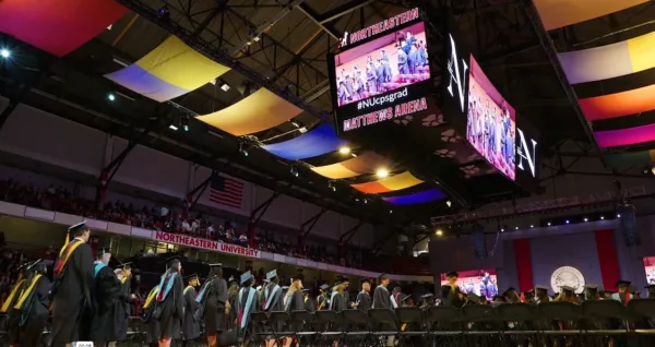 A group of graduates are standing in front of a large screen.