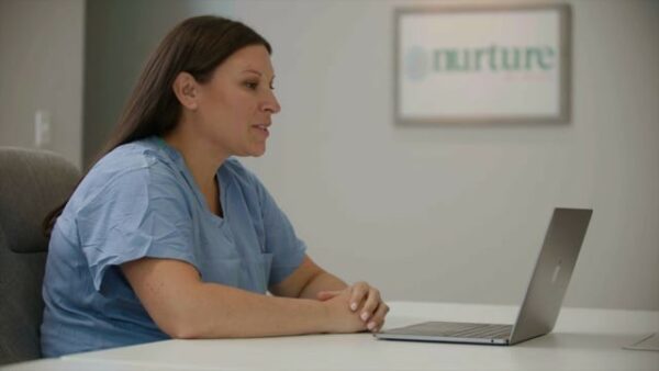 A woman in scrubs sitting at a desk with a laptop.