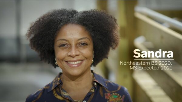 Sandra is a woman with afro hair standing in front of a building.