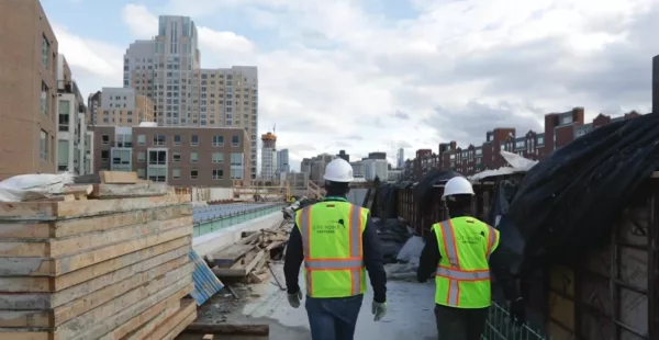 Two construction workers, employed by a Boston company, standing on a construction site.