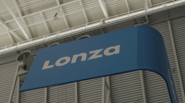 A blue sign with the word "Lonza" in white letters is displayed indoors against an industrial ceiling background.