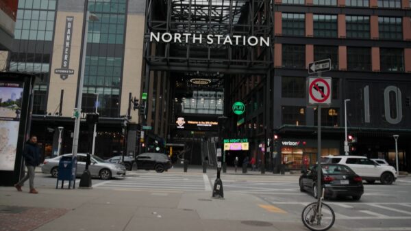 View of the entrance to North Station in Boston with cars, pedestrians, and a cyclist at a city intersection.
