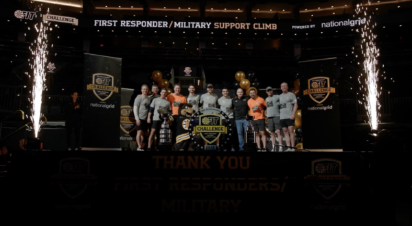 A group of people in athletic wear pose on a stage with banners and balloons at the First Responder/Military Support Climb event.