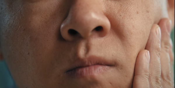 Close-up of a person's face, showing them pressing their cheek with their hand and looking slightly downward.